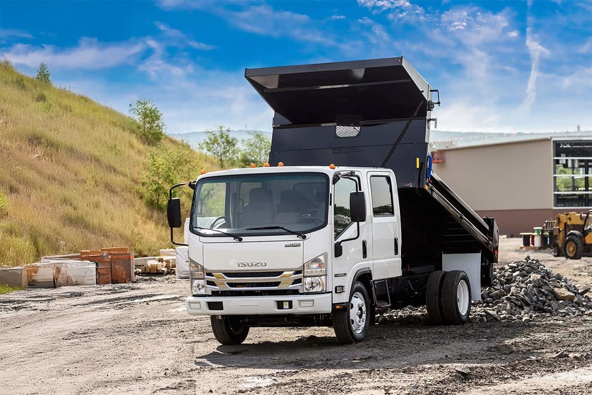 Isuzu NPR Crew Cab medium-duty truck dumping a haul in a gravel area