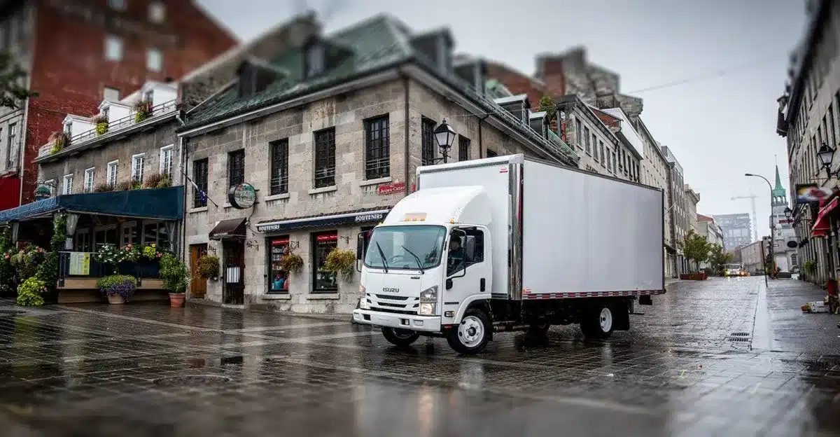Isuzu NPR HD medium-duty box truck driving in a city next to brick buildings