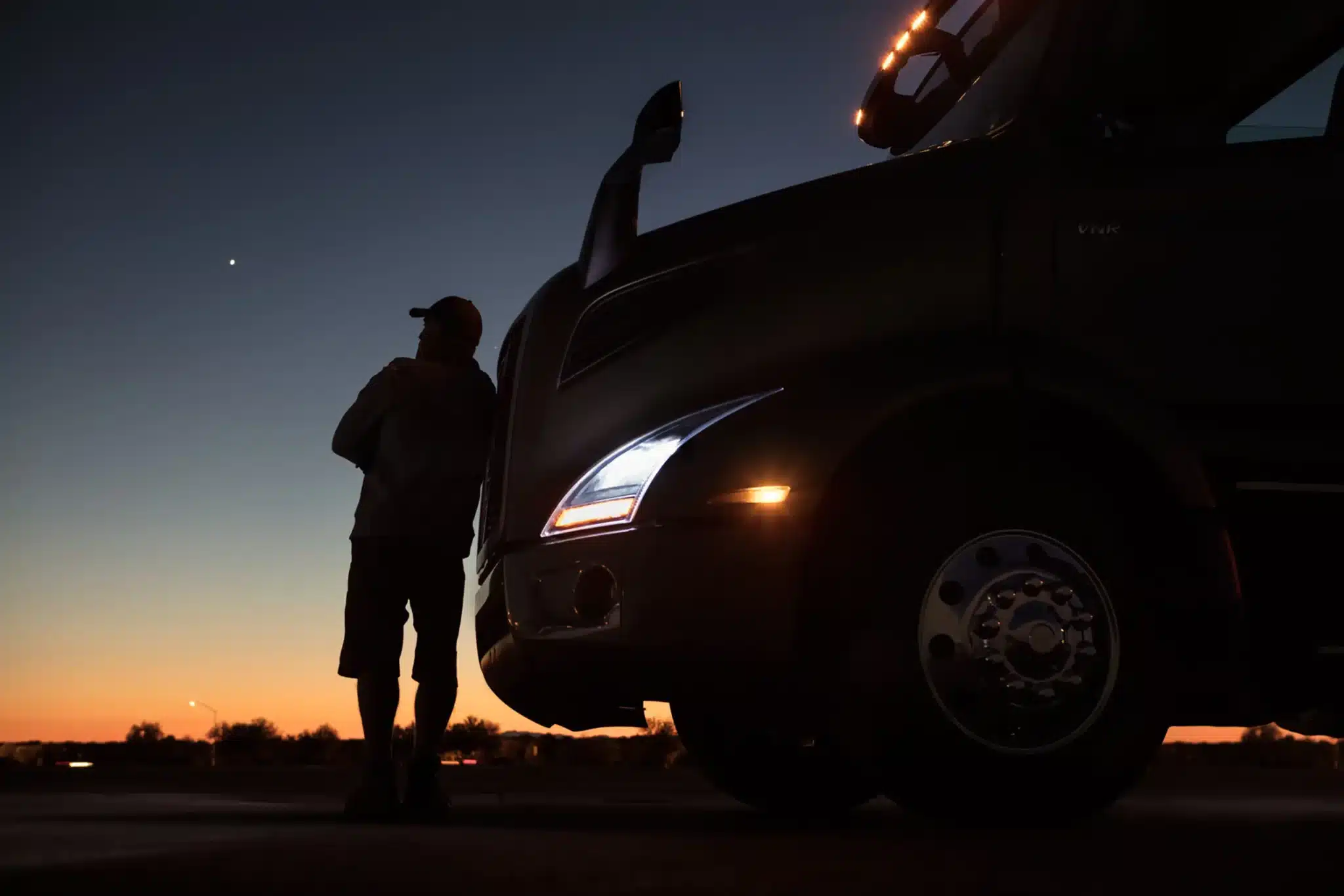 Silhouettes of a man leaning on the Volvo VNR 640 watching the sunset