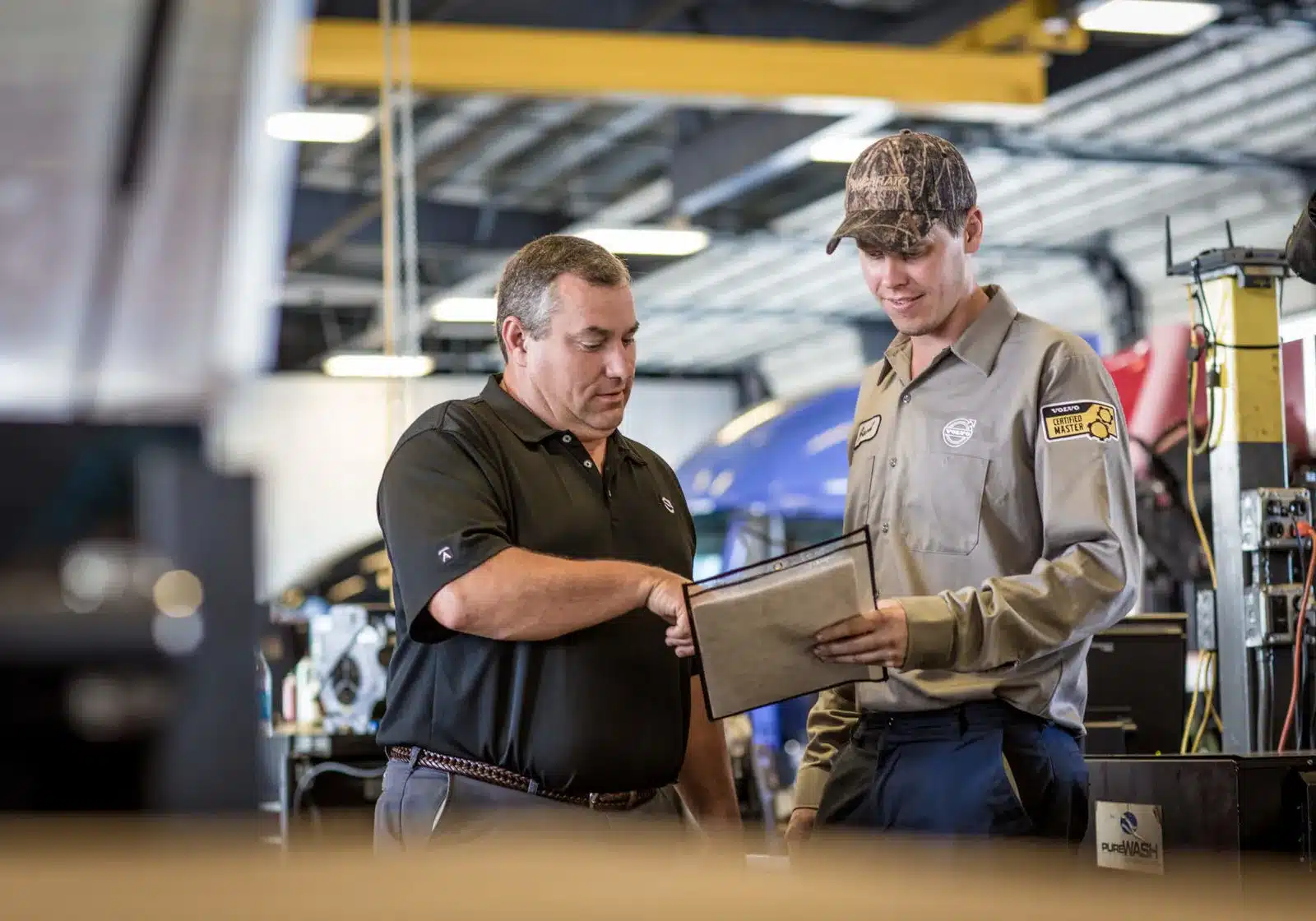 Technicians talking in a shop pointing at a clipboard.