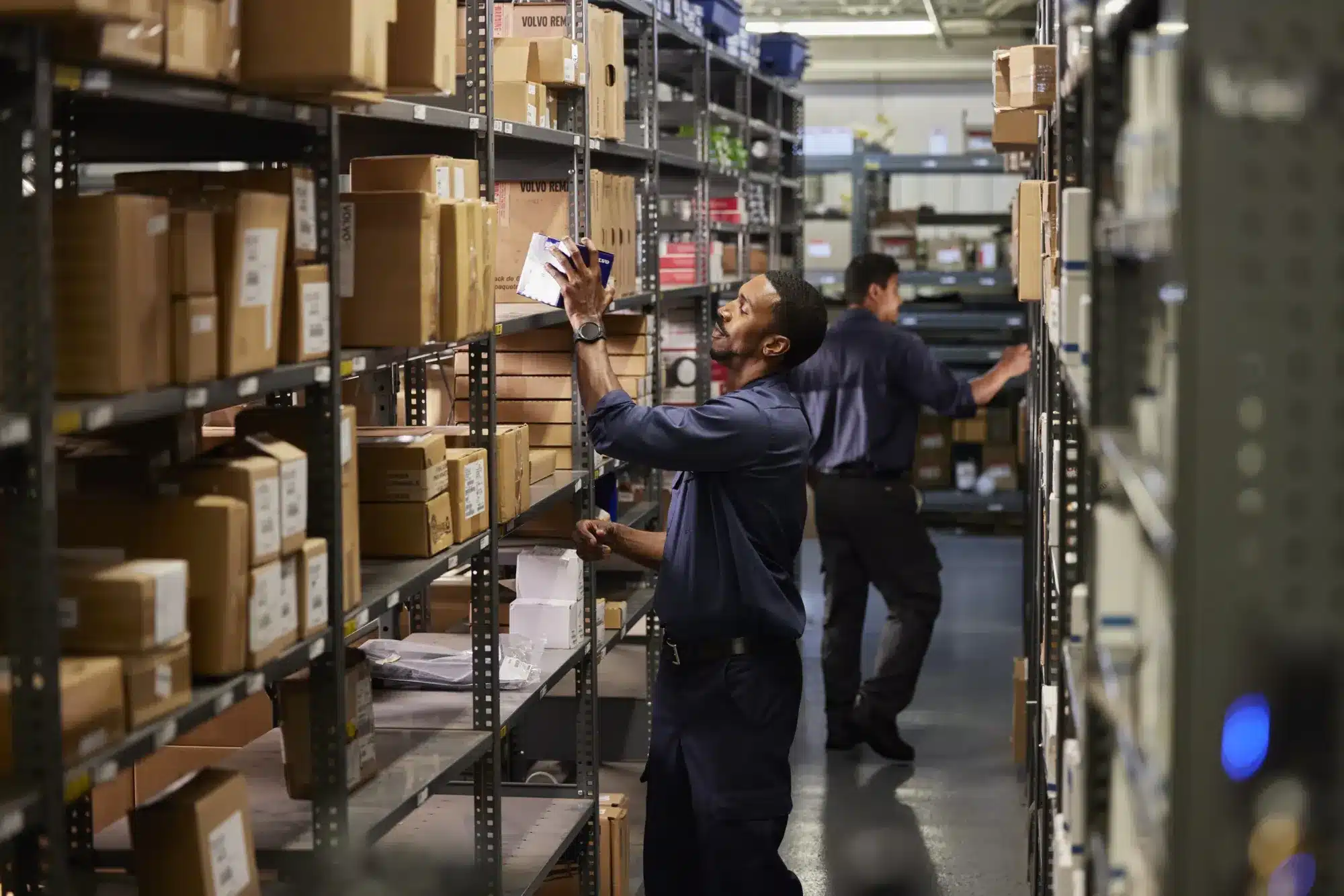 Man in parts warehouse grabbing a box of parts from the shelving.