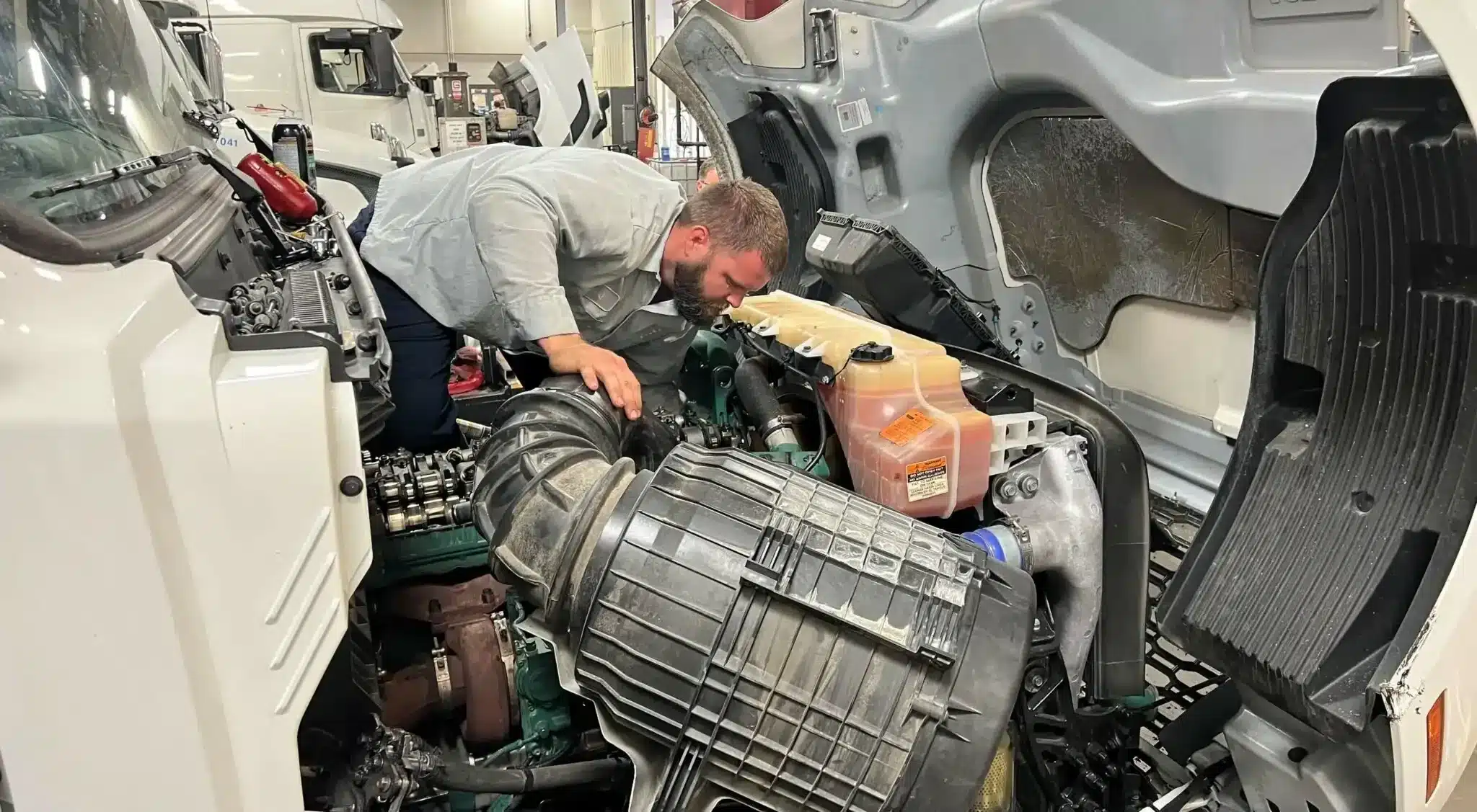 Technician bending over to look into a semi truck engine.