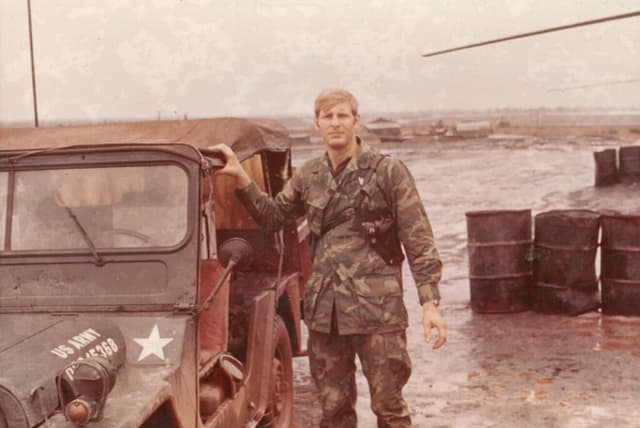 Young David Thompson in a military uniform standing next to a military jeep