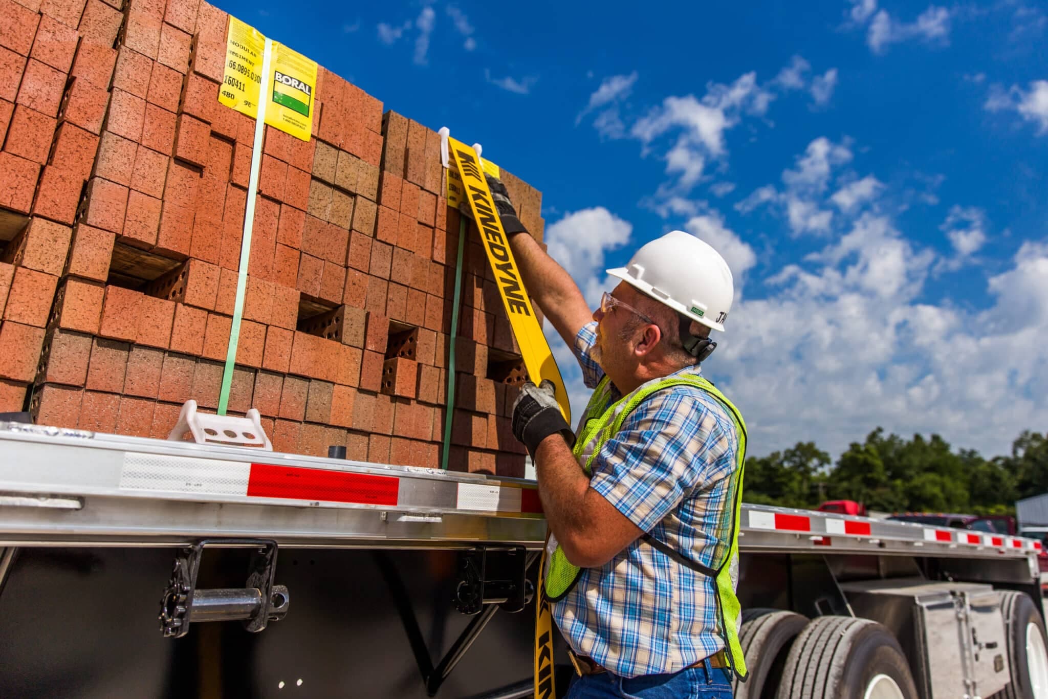 Man in a striped shirt and hard hat securing cargo on a flatbed trailer