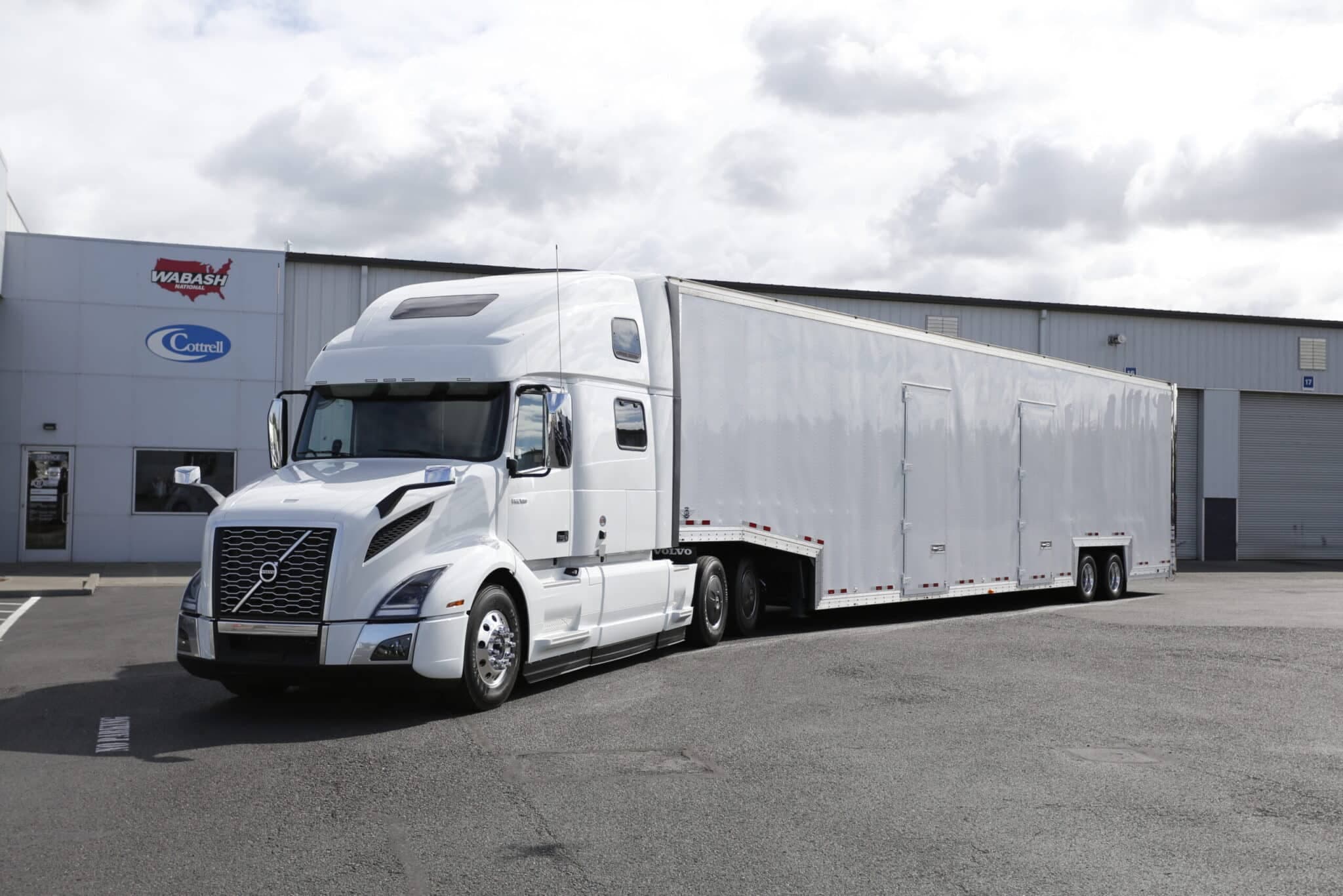 A white Kentucky enclosed trailer attached to a white Volvo VNL 860 in front of a TEC Equipment building