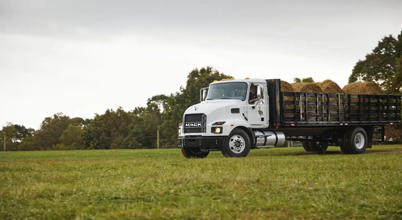 A white Mack MD stakebed driving through a field