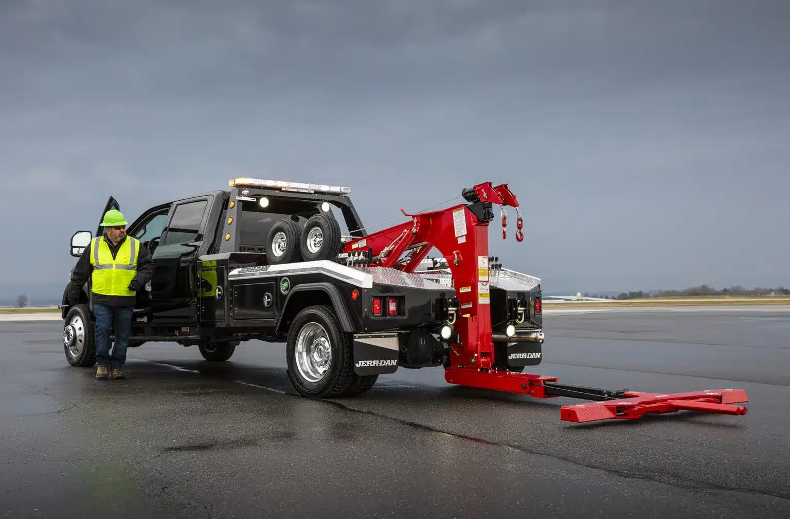 Black Jerr-Dan Wrecker in a parking lot with an operator walking towards the back of the truck