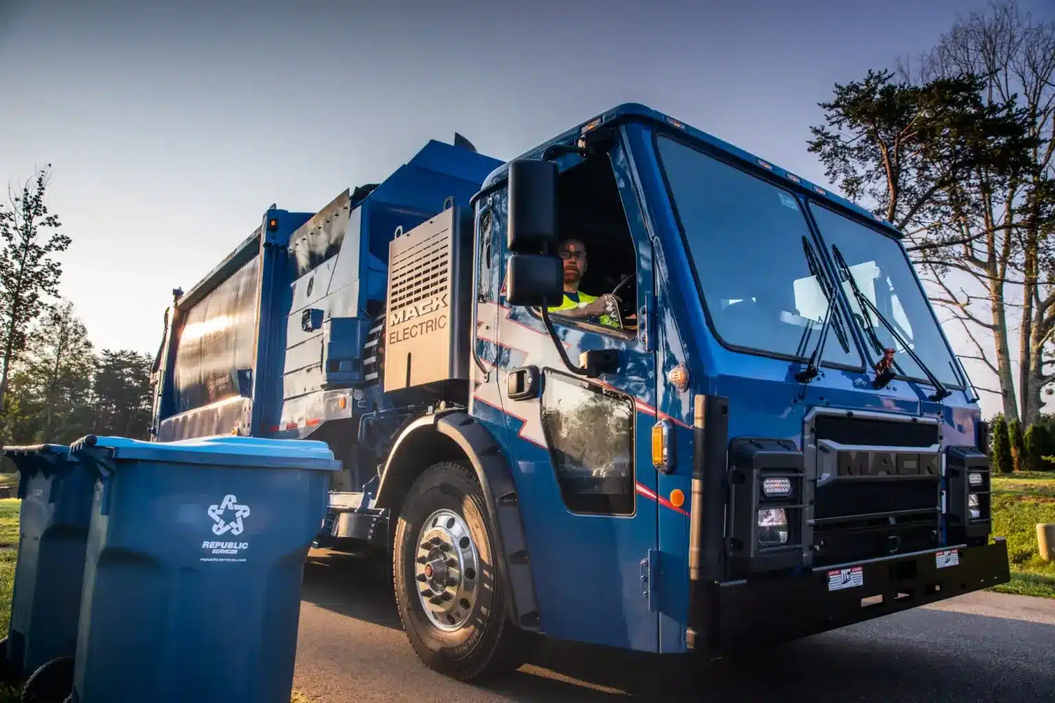 Blue Mack LR refuse truck parked next to recycling bins