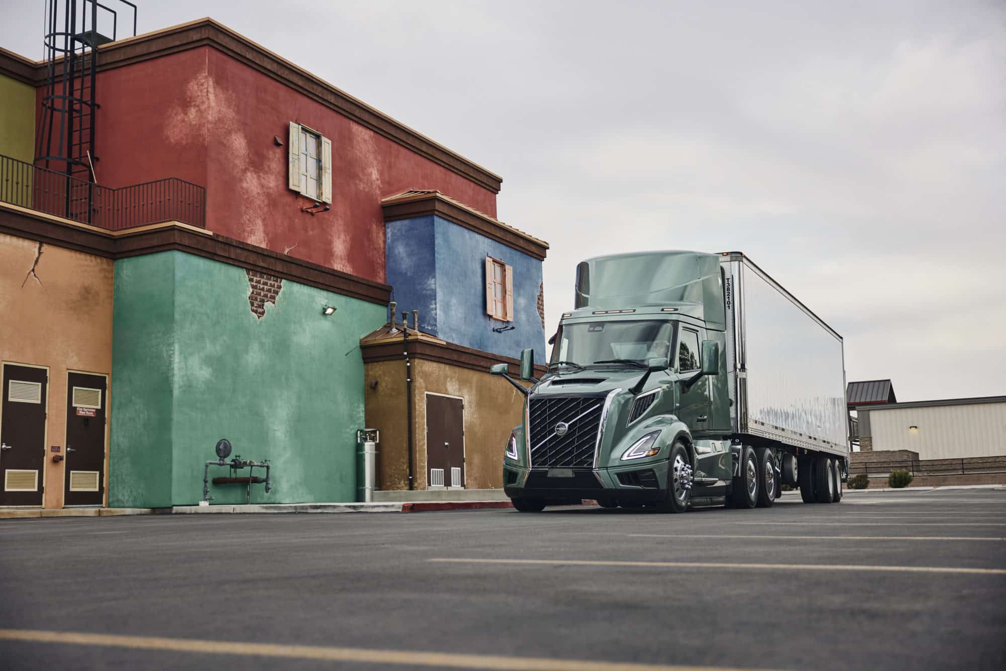 Green all-new Volvo VNL 300 with a dry van parked next to a multicolored building