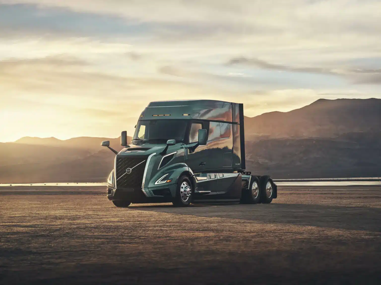 Green all-new Volvo VNL 840 midroof sleeper parked in a dessert with mountains and water in the background
