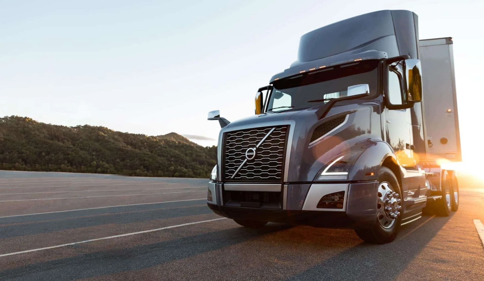 Volvo day cab on the road with sun shining behind it.