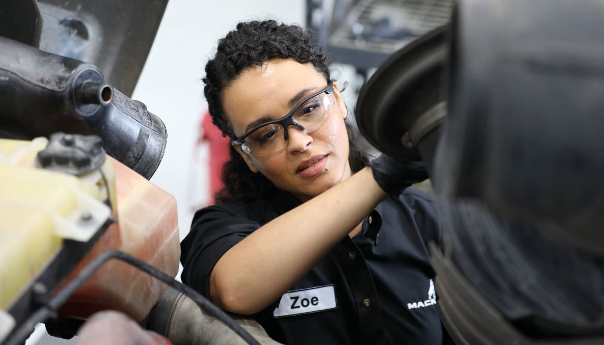 A woman technician up close with the hood open of a truck looking at the engine.