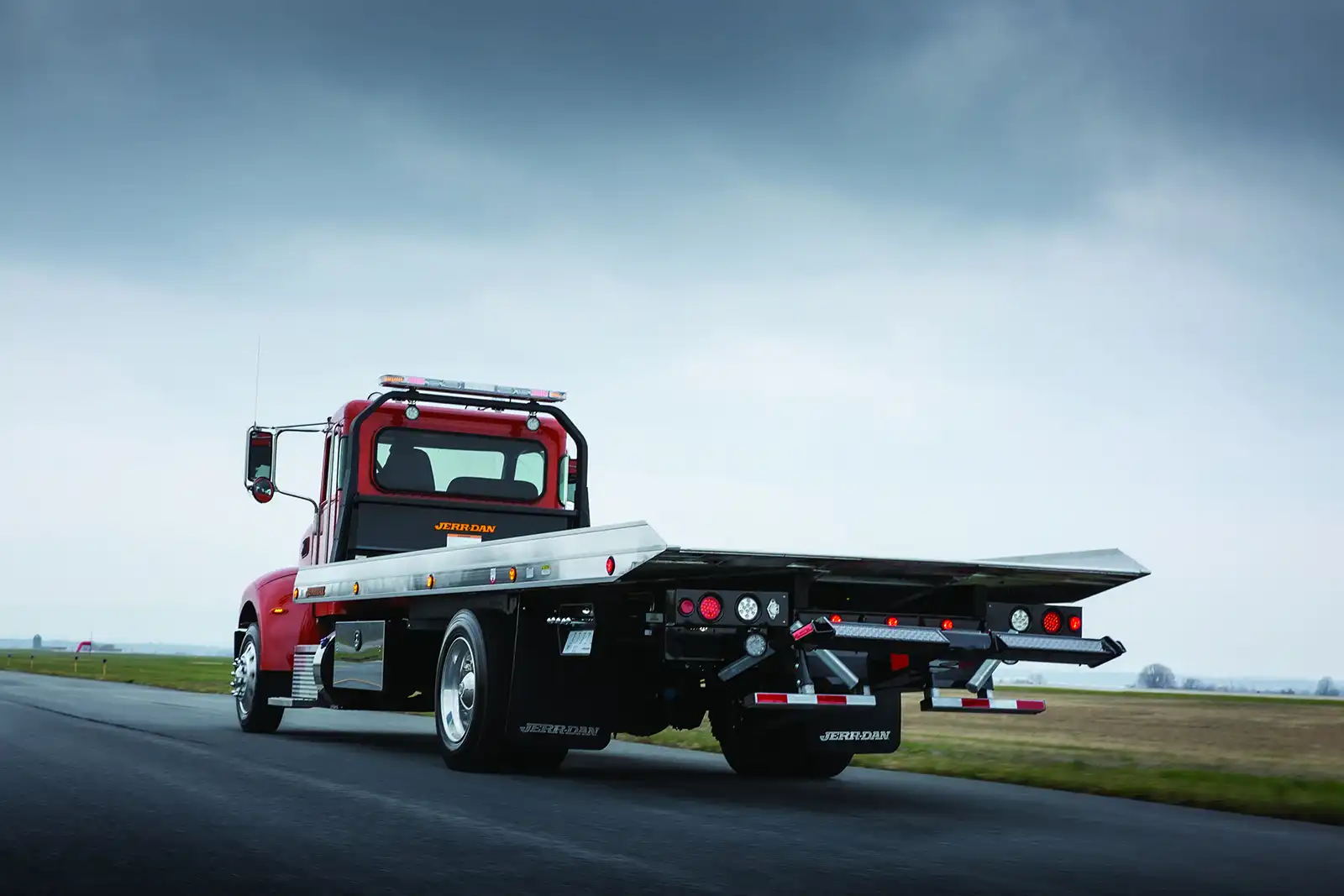 A red Jerr-Dan carrier driving down a road