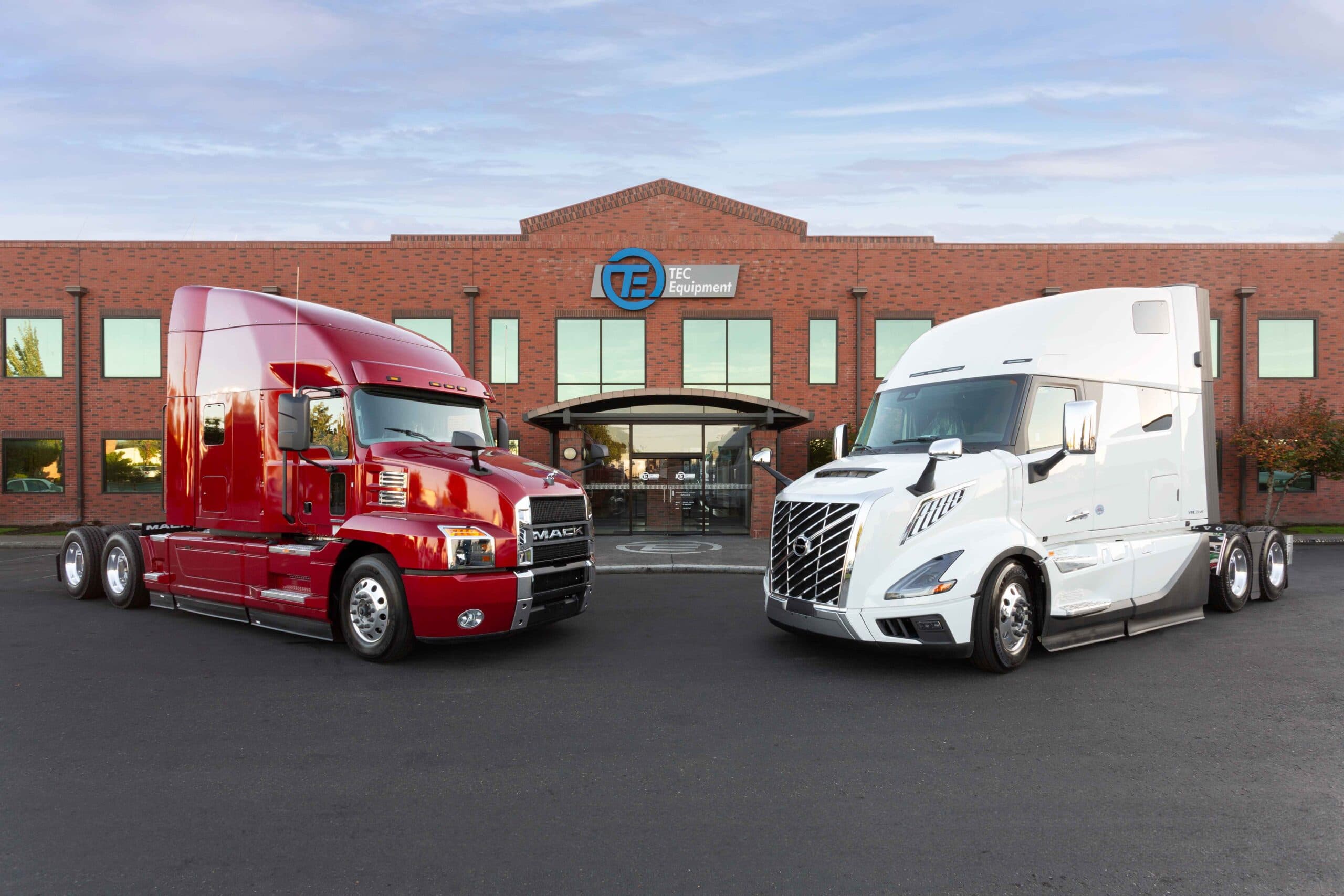 A red Mack Anthem and a white all-new Volvo VNL 860 in front of TEC Equipment headquarters.