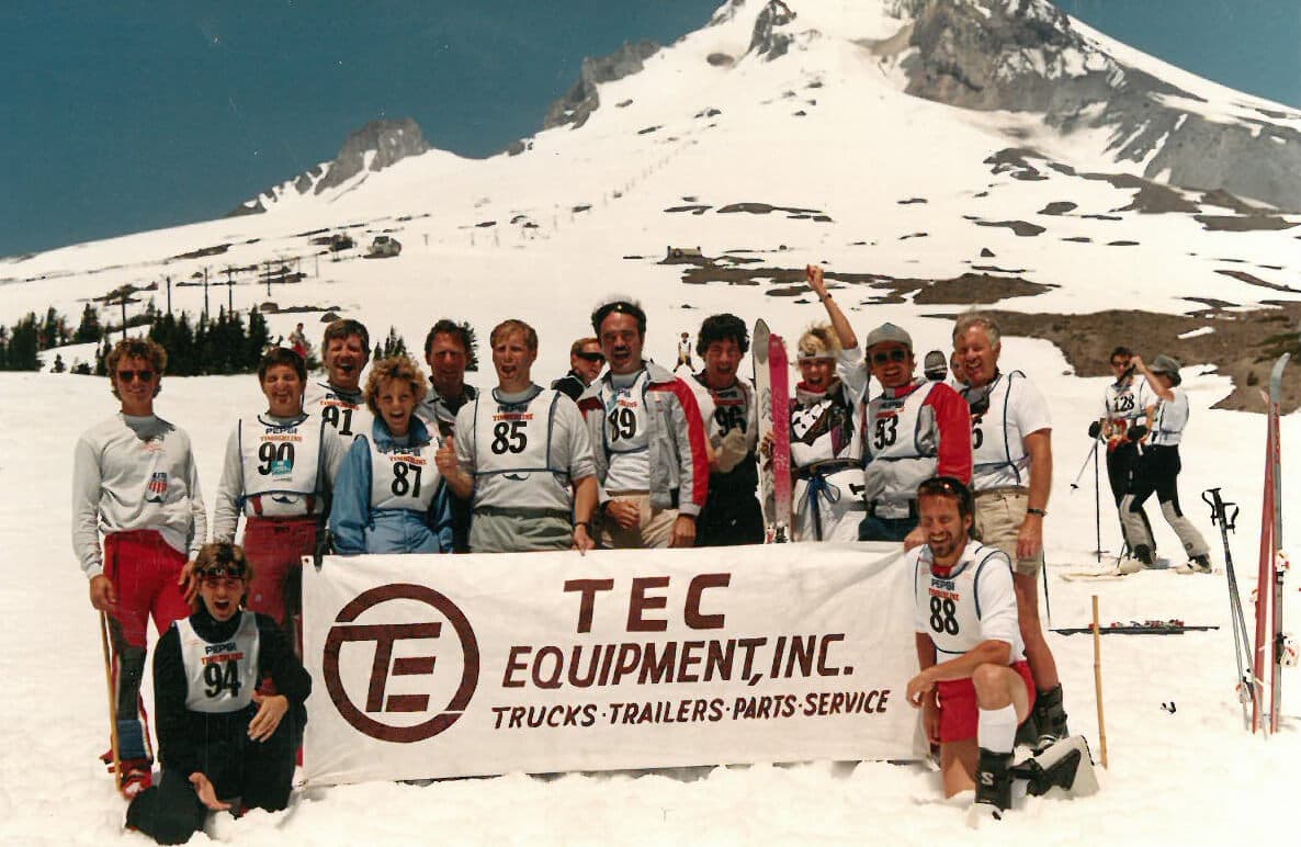 Group of TEC Equipment employees on the base of a ski hill holding a sign